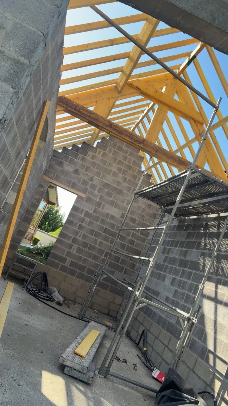 Charpente en bois neuve à fermettes sur murs en parpaings, échafaudage intérieur, vue en contre-plongée au soleil