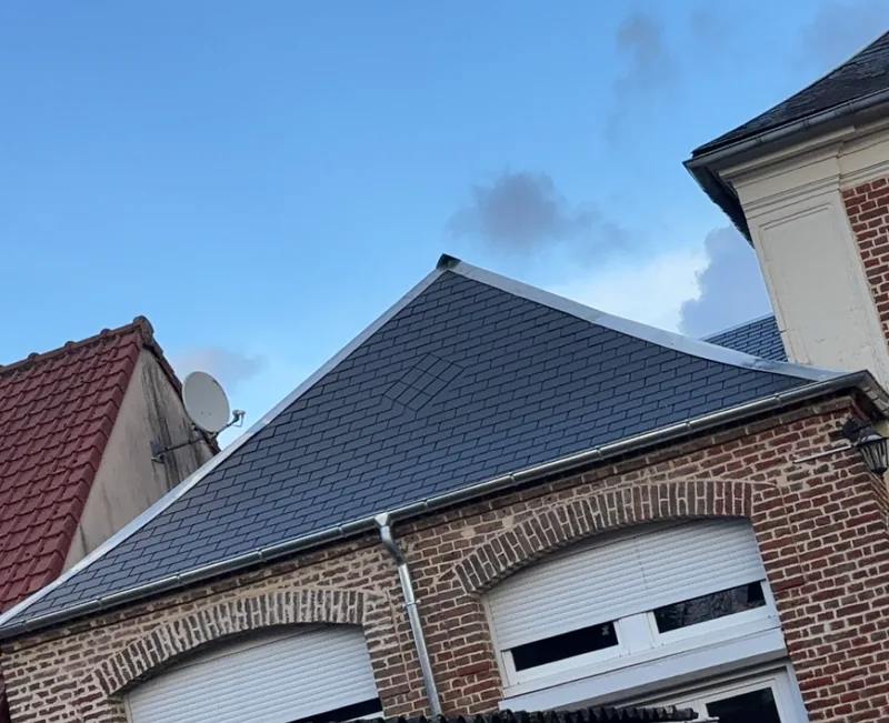 Toit en ardoise neuve à quatre pans sur une maison en brique rouge, volets roulants blancs, ciel bleu