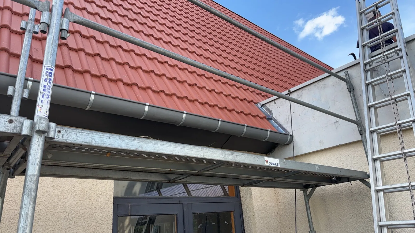 Toit en tuiles rouges neuves avec gouttière en zinc neuve, échafaudage au premier plan, ciel bleu